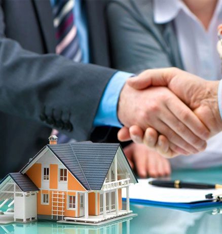 Two people shaking hands over a table with a model of a house.